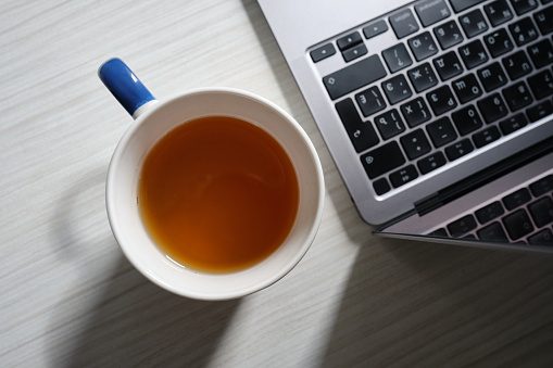 Laptop and a cup of hot tea on the table. Working atmosphere. A means of modern communication. On a white distressed table top