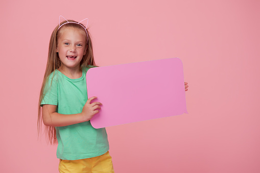 A cute laughing child girl is holding a signboard with an empty space for text. Advertising of childrens products and the announcement of discounts and sales