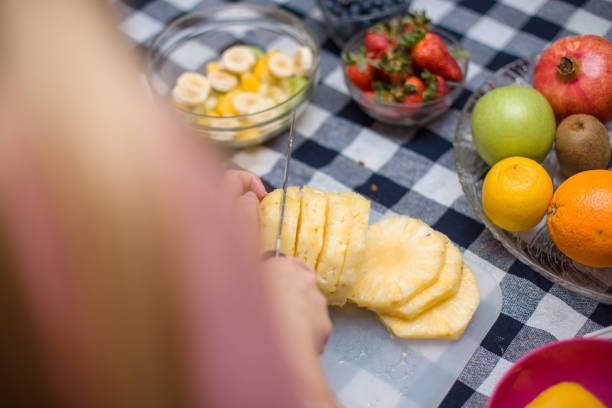 młoda dziewczyna pokazująca, jak wyciąć ananasa - fruit salad fruit healthy eating making zdjęcia i obrazy z banku zdjęć