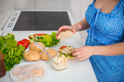 Young woman preparing sandwich. Salami slices, lettuce salad, cheese, butter, bread, bun, cucumber, sandwich sos and tomato. Top and side view