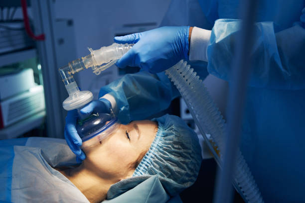 Anesthesia mask placed on the face of female patient Woman on the operation table getting anesthesia before the surgery. Doctor in medical clothes standing near anesthetic stock pictures, royalty-free photos & images