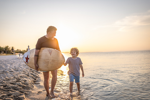 Photo of father and son walking along the beach after surfing day