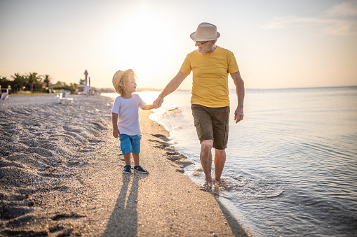 Photo of grandfather walking along the beach with grandson on a summer vacation
