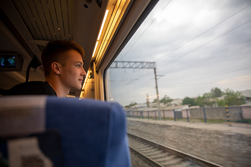 Profile view of a teenager boy riding on train, looking out of the window