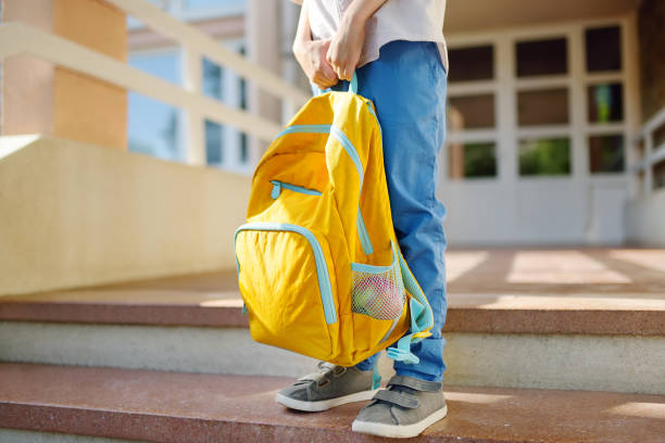 Little student with a backpack on the steps of the stairs of school building. Close-up of child legs, hands and schoolbag of boy standing on staircase of schoolhouse.Back to school concept. stock photo
