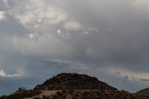 Dramatic sky and rainbow in Tucson, Arizona, near Mission San Xavier del Bac during monsoonal rainstorm with the rainbow seemingly emanating from the cross