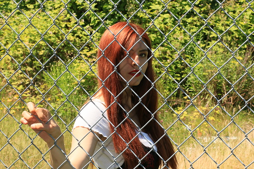 A Mexican woman behind a chain link fence. She is wearing a short sleeved white shirt and a black skirt.