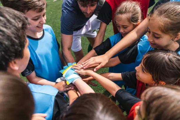 Female and male kids soccer players together with hands in circle before a match. High angle view