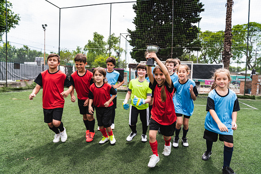 Group of kids celebrating together the winning of a competition running on a soccer field. Boys and girls together. Two different teams celebrating together.