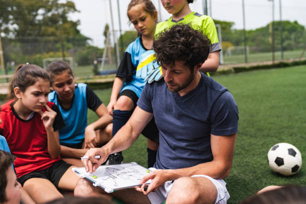 niños de un equipo de fútbol escuchando a su entrenador, sentados juntos en un campo de fútbol - campeonato deportivo juvenil fotografías e imágenes de stock
