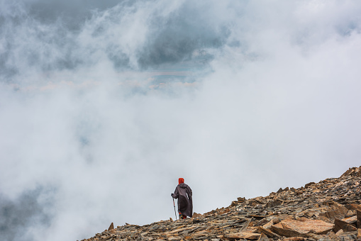 Awesome mountain landscape with hiker at very high altitude in dense low clouds. Wonderful alpine scenery with man on stone hill among sharp stones in thick clouds. Man and majestic mountains nature.