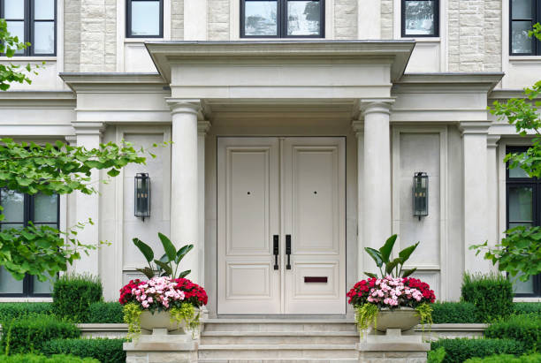 House entrance with white double doors columns surrounded by pots of flowers stock photo
