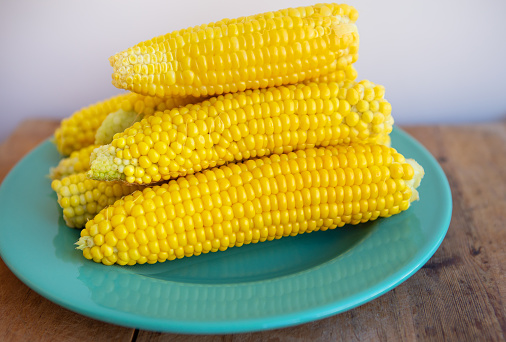Boiled corn cobs lie on a green plate. Delicious and juicy corn