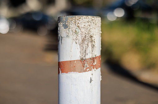 Old white metal bollard with a road behind.