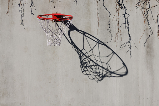 Old red basketball hoop with ragged net attached to a wall with shadow pattern.