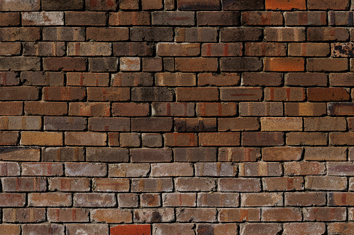 weathered, grungy and dirty bricks in a wall. Structure is regular and cement is used in the gaps.