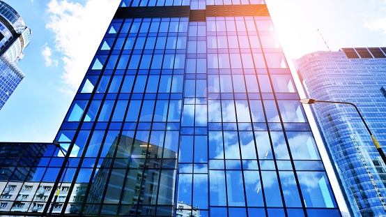 Transparent glass wall of office building. Bright sunny day with sunbeams on the blue sky.Velvia graphic filter