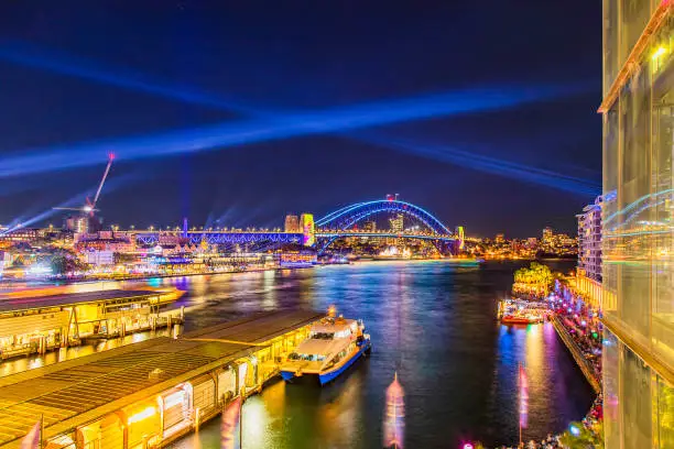 Circular quay ferry wharves at Vivid Sydney 2022 light show festival with bright illumination of city landmarks.