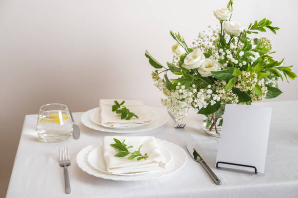 istock Mockup white blank space card for table number or menu. Wedding teble decoration with white flowers, glasses and white napkins. Elegantly decorated table at a wedding reception. Festive table setting. The wedding decor. 1407797820