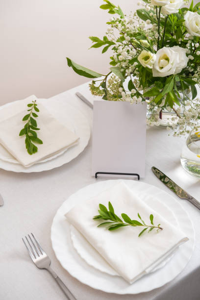 istock Mockup white blank space card for table number or menu. Wedding teble decoration with white flowers, glasses and white napkins. Elegantly decorated table at a wedding reception. Festive table setting. The wedding decor. 1407797828