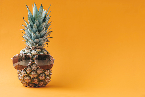 Pineapple wearing sunglasses in front of orange colored  background.