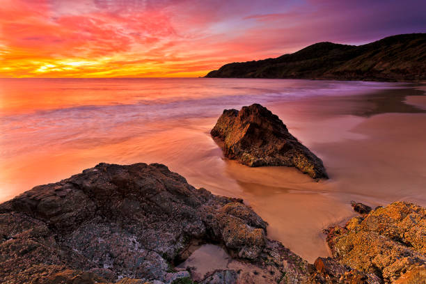 Bright hot red sunrise over Pacific ocean at Forster town Burgess beach with scenic rock cliffs and smooth sand.
