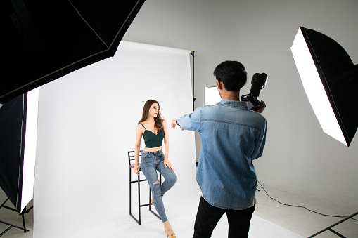 Model young woman posing for photo taken with professional photographer in studio on fashion concept. Photographer and model. Young man photographing fashion model.