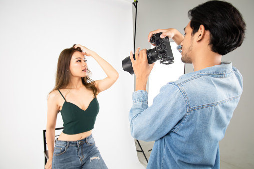 Model young woman posing for photo taken with professional photographer in studio on fashion concept. Photographer and model. Young man photographing fashion model.