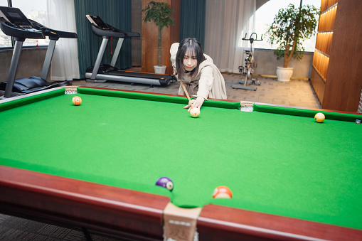 An Asian woman plays billiards in the billiard hall