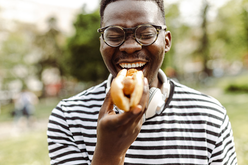 Young African American man is eating a hot dog and enjoying