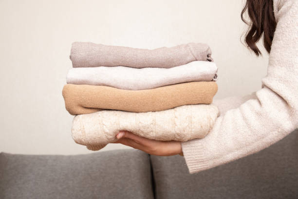 istock Stack of cozy knitted sweaters in female hands on sofa background. Warm concept 1407817673