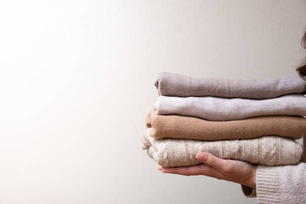 istock Stack of cozy knitted sweaters in female hands on beige background. Warm concept 1407817861