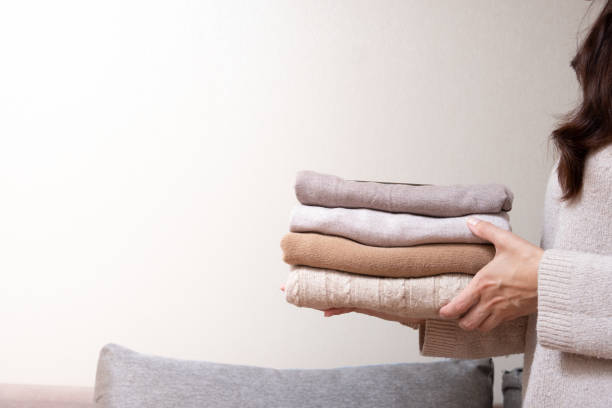istock Stack of cozy knitted sweaters in female hands on sofa background. Warm concept 1407818393