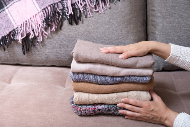 istock Female hands stack cozy knitted sweaters on the sofa with blanket. Warm concept 1407819338