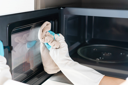 Woman hand with microfiber rag cleaning inside of microwave oven in kitchen at home. Closeup