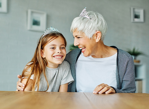 Daughter or granddaughter surprises her mother or grandmother with present a princess crown toy on mother's day or birthday at home