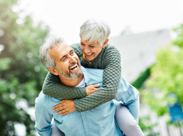 woman man outdoor senior couple happy lifestyle retirement together smiling love piggyback active mature Happy active senior couple outdoors senior lifestyle stock pictures, royalty-free photos & images