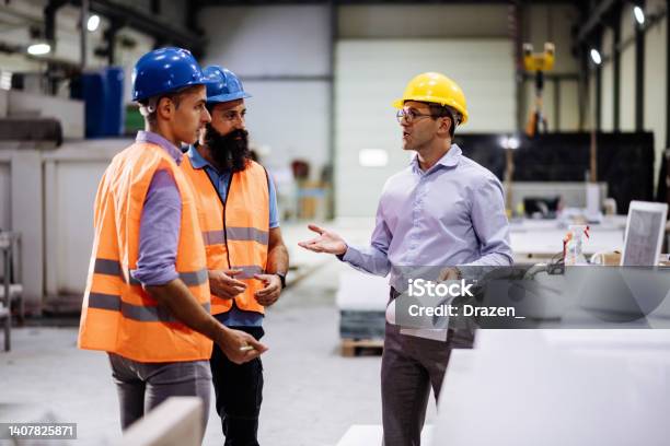 Engineers In Factory Hall Performing Quality Control Manufacturing Occupation In Modern Industrial Hall With Automated Process And Robots Metal Processing Industry And Warehouse Stock Photo - Download Image Now