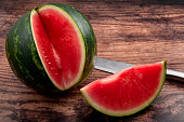 Vitamin rich fruits and summertime refreshment concept with photograph of perfect seedless watermelon slice and metal knife isolated on rustic wood background