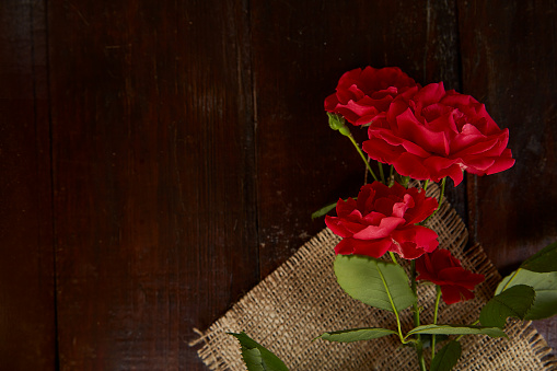 Red roses background on sacking on wooden background. Present, gifting. Copy space.