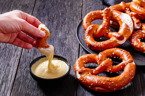 woman dips a piece of pretzel in cheese sauce, horizontal view from above, close-up