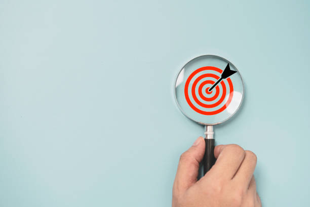 istock Hand holding magnifier glass with dartboard with arrow for focus and setup business objective target and goal concept. 1407830202