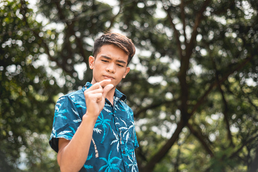 A twenty-something Filipino man looks at his index finger and thumb, making a small measurement expression.
