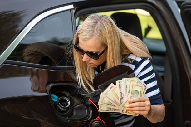 donna preoccupata con i soldi in mano guardando il serbatoio dell'auto aperto, il concetto di aumento dei prezzi del carburante - gasoline fuel pump women currency foto e immagini stock
