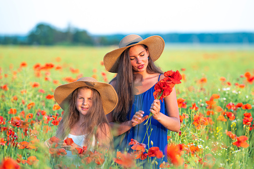 pretty young woman with girl in straw hats in poppy field, happy family having fun in nature