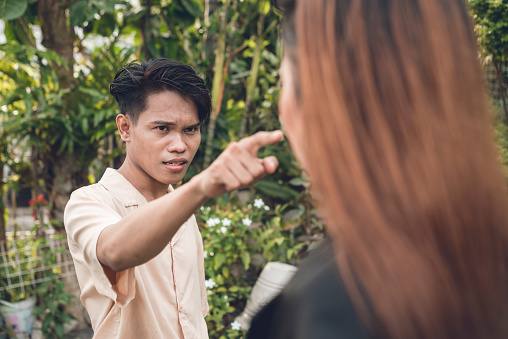 An irate Filipino man accuses his girlfriend of infidelity. Scolding and berating her. Outdoor scene.