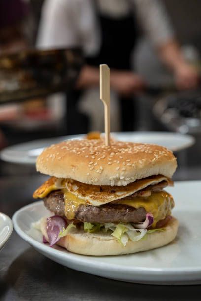 istock Restaurant kitchen imagery with a freshly prepared cheeseburger resting on a plate and a busy chef in the background 1407834022