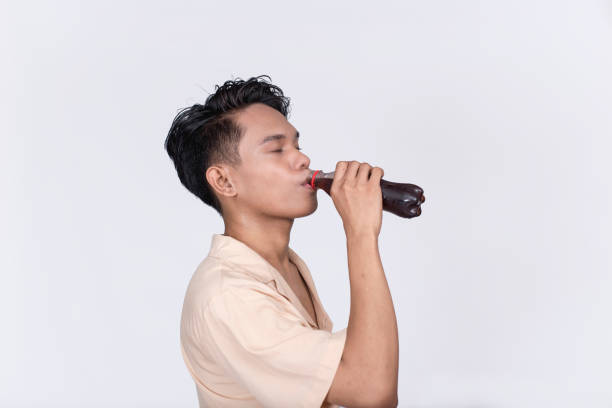 istock A young asian guy drinks a PET bottle of cola. Isolated on a white background. 1407834058