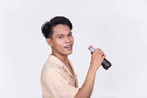 A young asian man expresses satisfaction after drinking a PET bottle of cola. Isolated on a white background.