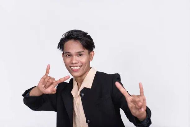 A smiling man in his 20s making a rock on gesture with both hands. Energetic and upbeat. Isolated on a white backdrop.